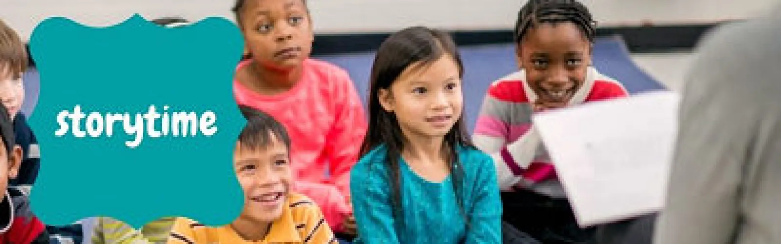 Several children in a diverse group sitting on the floor, listening to an adult read a story. The caption reads storytime